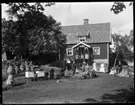 Det nya bostadshuset i Brevik med bikupor framför. Familjen med gäster och ett får finns också på bilden. Okänd, Okänd, Johan Pettersson, Hjärtum 1868-08-01, Agnes Johansson, Hjärtum 1918-08-05, Allan Eriksson, Hjärtum 1913-03-21, Charlotta Pettersson, (född Larsdotter) Väne Ryr 1858-04-15, okänd, okänd, Signe Johansson, Hjärtum 1896, Hilda Johansson, Hjärtum 1900-04-27, okänd, okänd