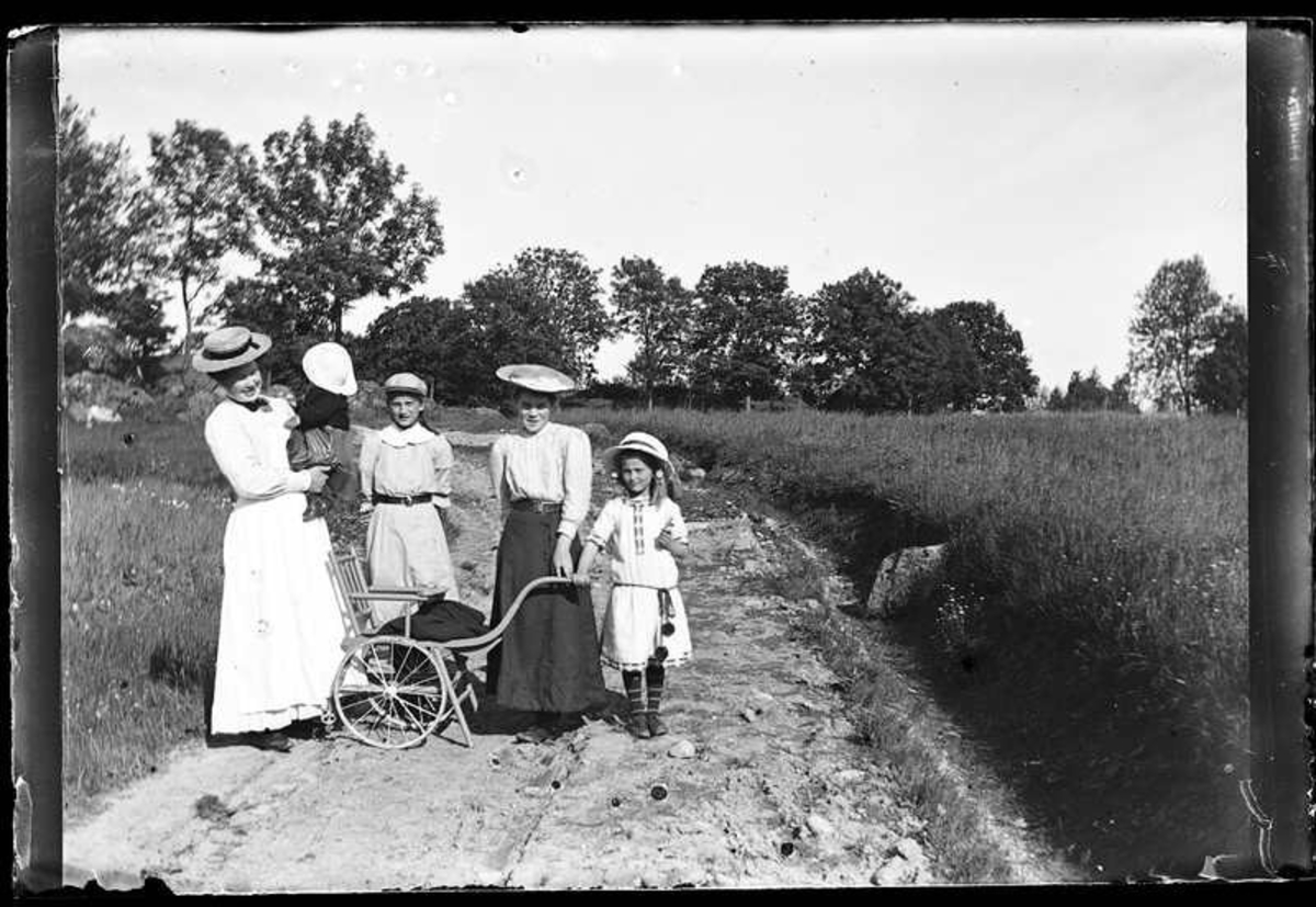 Olof Jonssons text: "Jenny Andersson, Karlinders barn med barnjungfru, 27 juni 1909."

Jenny Andersson, Hjärtum 1884-10-10, Lars Gustaf Karlinder Trollhättan 1908-06-05, Anna Lisa Karlinder Högbo 1896-06-25, okänd, Ingeborg Margareta Karlinder Trollhättan 1901-04-23. Fotot är taget på vägen fram till Brevik.