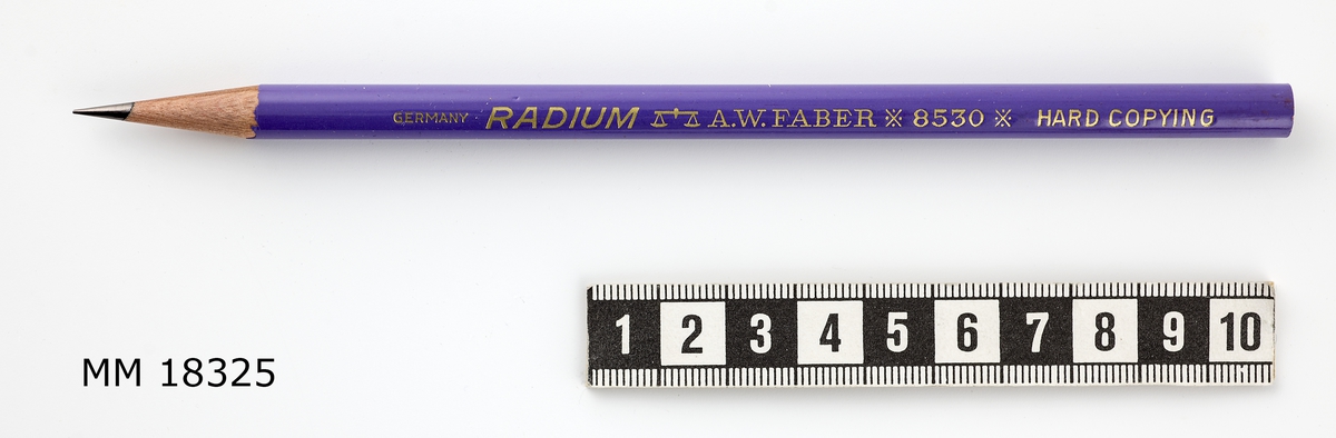 Penna med anilinstift av trä, rund form, lackad i lila. Längs pennan instansad text färgad i guld: " TILLHÖR STATSVERKET " samt  " GERMANY RADIUM / vågsymbol / A.W.FABER *8530* HARD COPYING ". Vässad till spets i pennformerare.