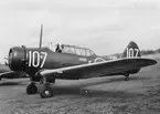 Flygplan SK 14A märkt nummer 107 med flygförare står på ett flygfält. Flygplanet tillhörande Krigsflygskolan F 5.