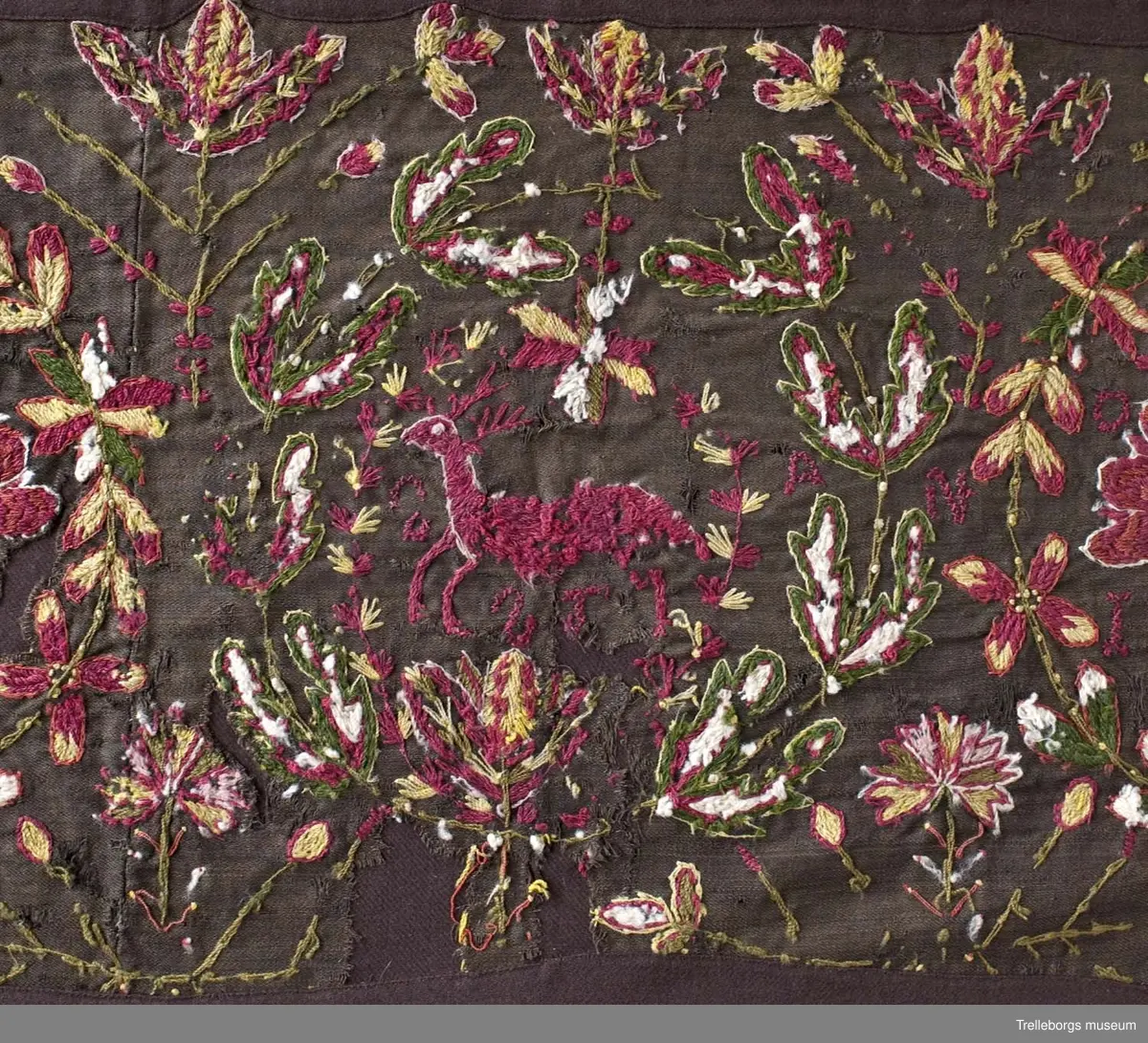 Broderad agedyna på mörkbrun botten. Motivet är tre stora blomkransar, de två yttersta har varsin rutig blomvas med tre blommor i, samt bokstäver PHH  OPZ, i den första och årtalet 1890 i den sista. I den mittersta kransen springer en stor röd hjort med röda horn. Även här finns bokstäver, två bakvända S och ett T. Färgerna går i rött, gult, grönt, vitt och blått. Utanför blomsterkransarna fortsätter blommor att växa upp.