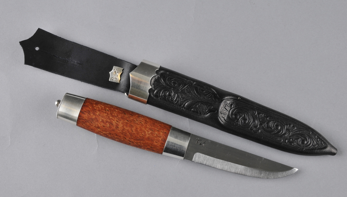Kniv med slire. Slira er trykt og læret er tysk rårand. Øverst er det ein sylvholk med ein spiss oppover i front og ein svak profilering i underkant  Knivskaftet er laga av valbjørk med sylvholkar oppe og nede. På toppen av holken er det ei svakt boga, oval sylvplate med ein sylvkule på toppen og åtte gravera strekar ut mot kanten som har ein tvinna slyvtråd (filigran) som avslutning. Knivbladet er laminert jarn og stål.