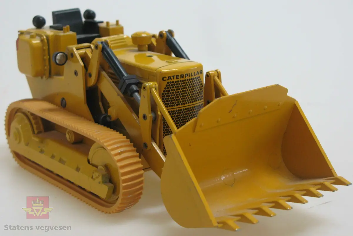 Leketøy, miniatyr beltelaster, Caterpillar 941. Lagd av metall og gummi. Gul med enkelte svarte detaljer. Lasteren går på belter, har skuffe foran og trekkfesta bak. Mangler trolig bøyle eller hytte over førerplassen. Merking fra produsenten under leketøyet samt Caterpillar merking utenpå.