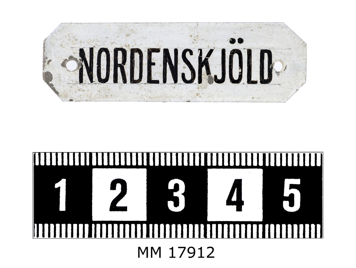 Rekangulär skylt av plåt med avklippta hörn. Framsidan vitmålad och försedd med handmålad text i svart: " NORDENSKJÖLD ". Hål i kanterna för spikar.