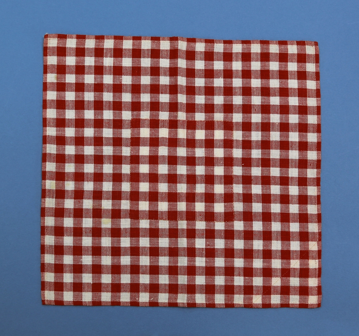 Firkantet tøylapp kantsydd for hånd og med lapp sydd på over hull