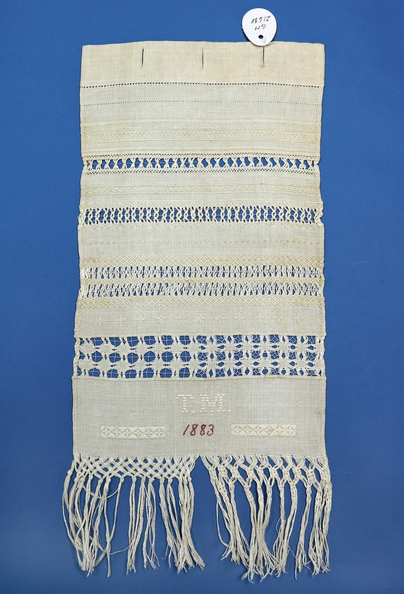 Avlangt lerretsvevd stoff med frynser nede og ulike sømteknikker, herunder broderi og uttrekkssøm