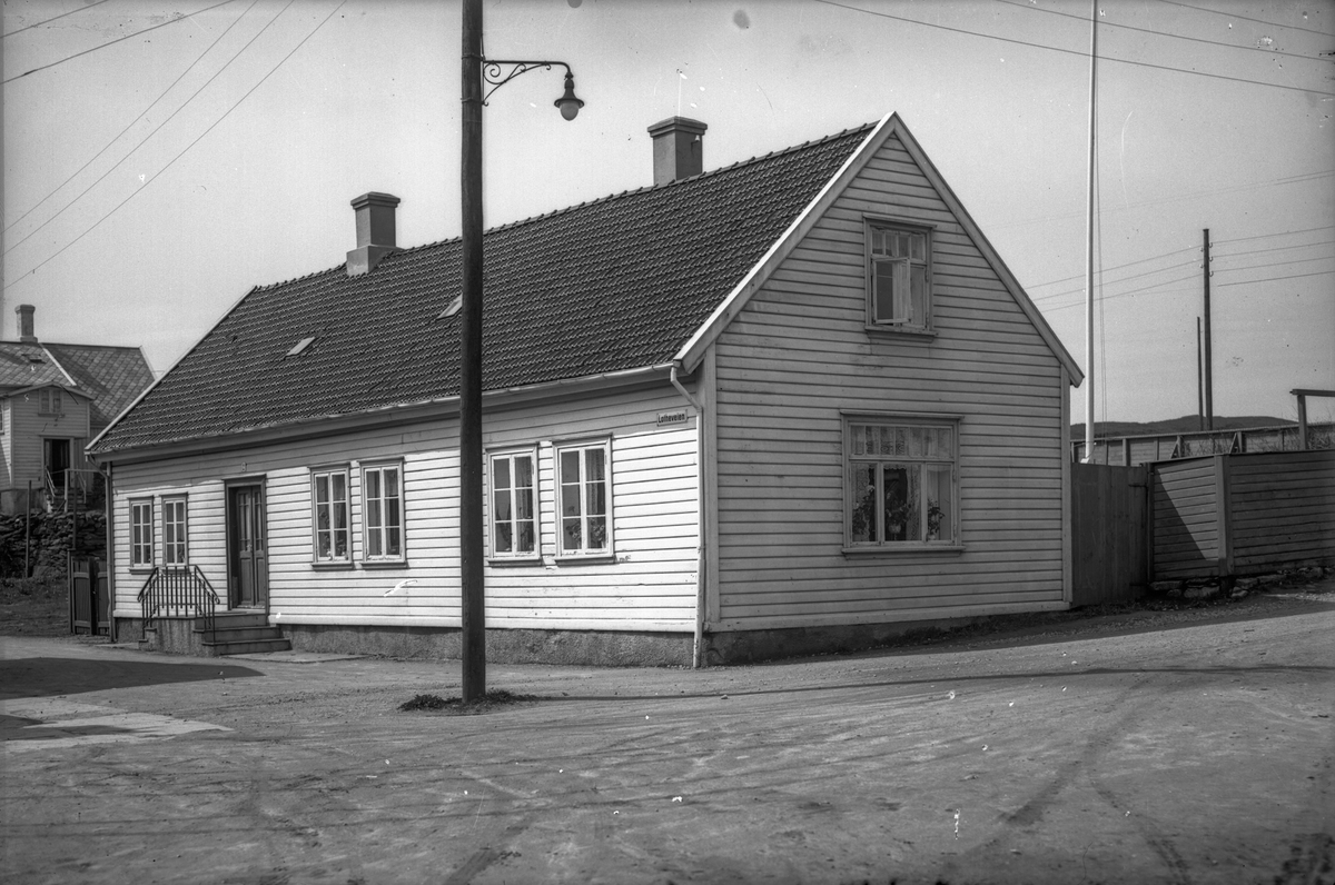 Uthus med to skorsteiner og en liten trapp på Hasseløy. En gatelykt. Fortau.