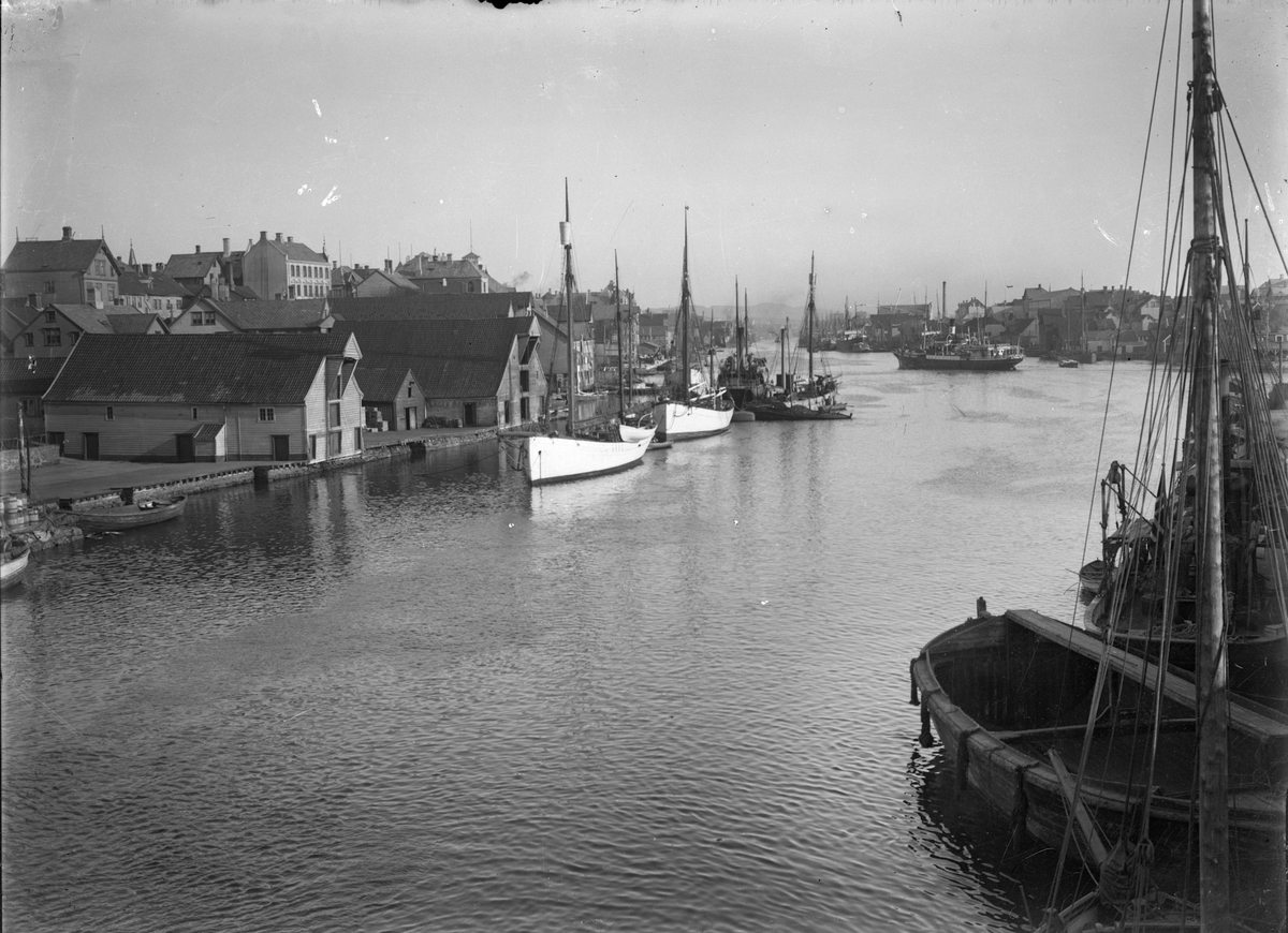 Smedasundet sett sydover fra Haugesund. Flere sileskuter og dampskip ankret opp på begge sider av sundet.  Dampskip i bakgrunnen. Sjøhus og trehusbebyggelse i bakgrunnen.