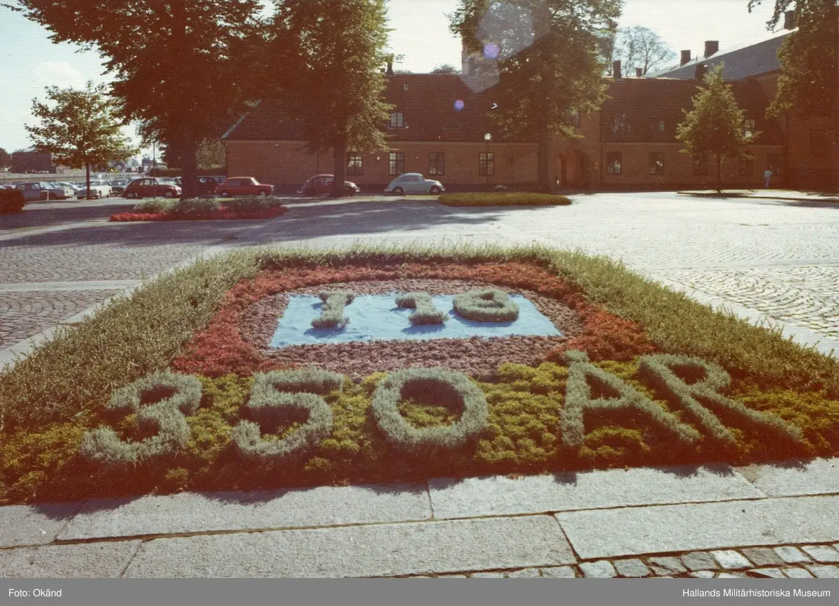 I dunkla färger skimrar stadens blomsterhyllning framför länets residens. 

I 16 350 År.