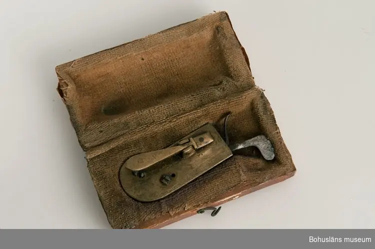 Ur handskrivna katalogen 1957-1958:
Snäppa
Snäppan a) L. 5,8 cm; mässing m. mekanismer av järn. Fodralet b) 7,2 x 3,7 x ,1 cm; trä, papper på utsid., tyg på insid. Trasigt.

Lappkatalog: 94