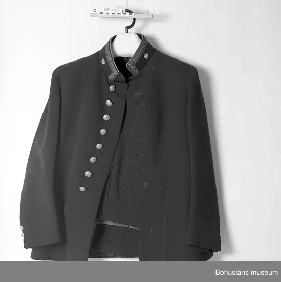 Livrock. Mörkblått kypertvävt ylle. Ståndkrage med kantband med eklövsblad i metallbroderi. Kunglig krona i mässing å ömse sidor kragens  knäppning. Livrocken knäppt framtill med åtta mässingsknappar med Göteborgs och Bohusläns vapen under hertigkrona. Tre dito mindre knappar på varje ärms nederdel. Avtagen i midjan. På ryggskjörtet tre par mässingsknappar som ovan.
Person- och tjänsteuppgifter se UM023787.
Se bilaga