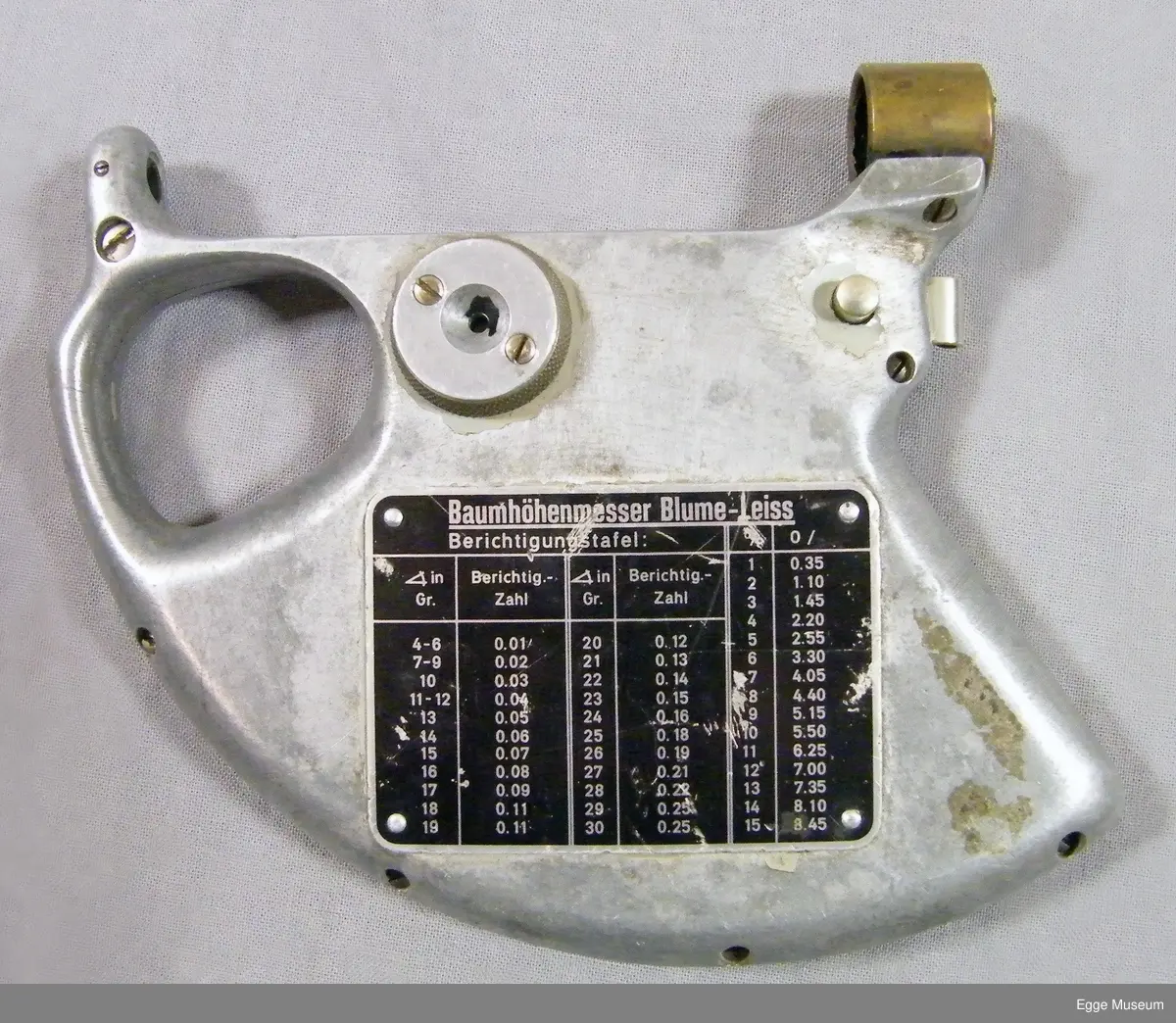 Høyemåler i lettmetal (aluminium?) med rektangulær skulderveske. Formen på instrumentet er omtrent en kvart sirkel. Instrumentet har gripehull i bakkant. Over gripehull er det montert et siktehull. I fremre kant er det montert en messingring, inne i denne ringen er det to spisse og triangulære spisser som stikker ut og peker mot hverandre. På ene siden av instrument er det montert et metallskilt med beregningsskala (ant tabellgrenser for avvik ved forskjellige målinger). På den andre siden er det en måleskale/avlesningsskala med en bevegelig pendel/fjær, dekt med gjenomsiktig plast.

Instrumentet er oppbevart i ei bæreveske av plasttrukket, grønt lerretsstoff. Veska har skulderreim i lær, som er poppet fast til vesken sider. Veska lukkes med lokk og låsestropp (denne er avslitt). Veska har to rom innvendig. Veska har muggskader på baksiden, samt at ene hjørnet i bunn har skader som har blitt sydd sammen.

Høydemåler for bruk på stående skog. Når man siktet inn toppen (eller rota) på treet som stod mellom disse punktene, og samtidig trykket inn en fjær, kunne man lese av vinkel og høyde, sett i forhold til en horisontal linje fra siktepunktet, i en måleskala på instrumentet. Man skulle vanligvis stå 20 meter fra treet. Høydemåleren er grålakkert, med noe avflassing. Av den tyske fabrikaten Blume-Leiss.

Brukt i undervisninga ved Skogskolen på Steinkjer.