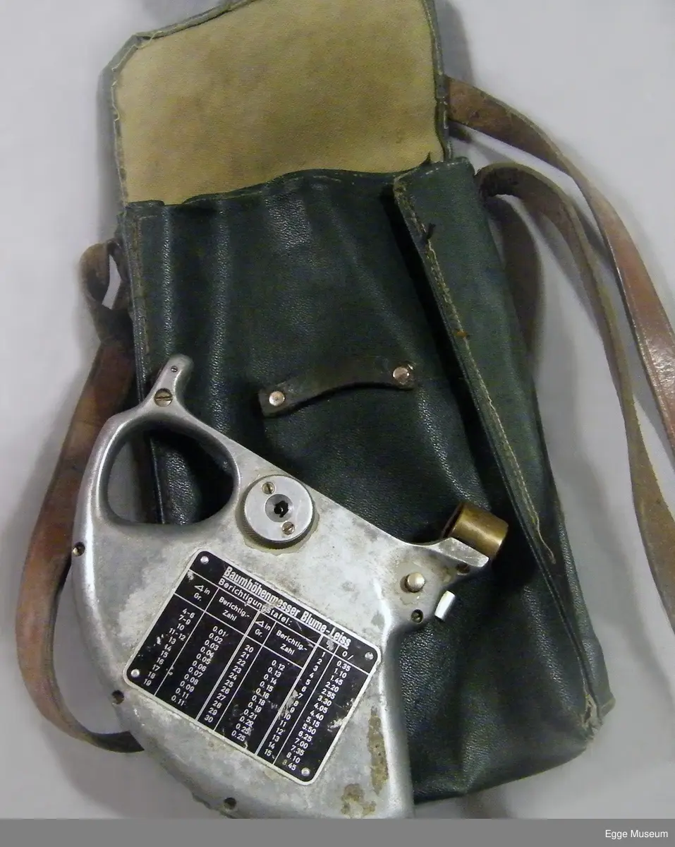 Høyemåler i lettmetal (aluminium?) med rektangulær skulderveske. Formen på instrumentet er omtrent en kvart sirkel. Instrumentet har gripehull i bakkant. Over gripehull er det montert et siktehull. I fremre kant er det montert en messingring, inne i denne ringen er det to spisse og triangulære spisser som stikker ut og peker mot hverandre. På ene siden av instrument er det montert et metallskilt med beregningsskala (ant tabellgrenser for avvik ved forskjellige målinger). På den andre siden er det en måleskale/avlesningsskala med en bevegelig pendel/fjær, dekt med gjenomsiktig plast.

Instrumentet er oppbevart i ei bæreveske av plasttrukket, grønt lerretsstoff. Veska har skulderreim i lær, som er poppet fast til vesken sider. Veska lukkes med lokk og låsestropp (denne er avslitt). Veska har to rom innvendig. Veska har muggskader på baksiden, samt at ene hjørnet i bunn har skader som har blitt sydd sammen.

Høydemåler for bruk på stående skog. Når man siktet inn toppen (eller rota) på treet som stod mellom disse punktene, og samtidig trykket inn en fjær, kunne man lese av vinkel og høyde, sett i forhold til en horisontal linje fra siktepunktet, i en måleskala på instrumentet. Man skulle vanligvis stå 20 meter fra treet. Høydemåleren er grålakkert, med noe avflassing. Av den tyske fabrikaten Blume-Leiss.

Brukt i undervisninga ved Skogskolen på Steinkjer.