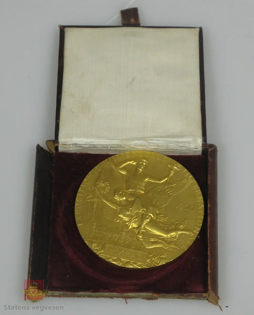 Medalje, laget av forgylt bronse. Preget med tekst og motiv på begge sider, også medaljørens navn. Medaljen ligger i et brunt etui med hvitt og rødt for.

Den ene siden har motiv knyttet til de olympiske leker, (Sommer OL i Paris i 1900). Vi ser to personer, den ene med fakkel i hånda og den andre har vinger som en mytologisk gud. I bakgrunnen ser vi Grand Palais, et stort bygg som ble reist til verdensutstillingen.
Den motsatte siden er preget med portrettet av et kvinnehode, kjent som Marianne. Etter den franske revolusjon ble Marianne gitt som navn til en kvinnefigur som symboliserte den franske republikken.