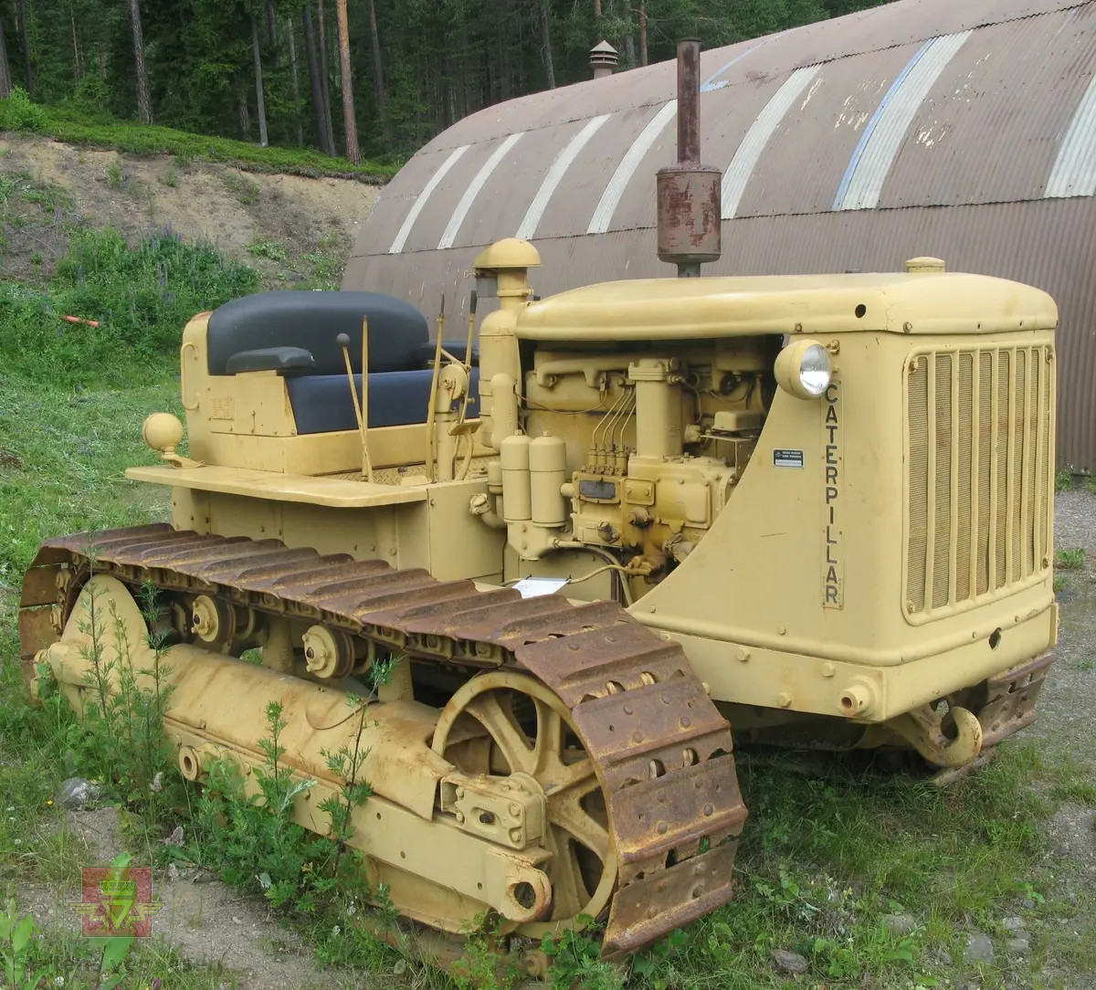 Caterpillar D 7. Gul, (opprinnelig grønn), med svart sete. Maskina er egentlig en bulldozer, men denne er bygget som beltetraktor. Forskjellen ser man best på den bredere fronten hvor det ikke er plasss til hydrauliksylindre for løft av bulldozerskjær. Denne har likevel hatt et skjær, men løfteanordningen som ble benyttet var vinsjen som satt bak på maskina. Wirene gikk fra vinsjen og over to tårn og videre ned på skjæret. Maskina har en 4-sylindret dieseldrevet motor som yter ca 128 Hk. Startmotoren er bensindrevet.
Oppstarting av dieselmotorene er såpass spesiell at den beskrives her:
Starteren er en 2-sylindret bensinmotor. Etter å ha skrudd opp bensinkrana og slått på tenningsbryteren på ON, settes sveiva ned gjennom panseret. Choken må setes på etter behov og gasspjeldet må settes på litt over tomgang. Startmotoren dras over komp. til den starter. Startmotoren bør gå noen minutter fordi avgassene varmer opp dieselmotorens innsugningsrør. Dieselmotorens gasshåndtak settes på halv gass, og dekompresjonshåndtaket på siden av motoren settes til, (slik at motoren går lett rundt).
Det finnes to håndtak for å koble til driften mellom starter og hovedmotor, det ene for å flytte "bendixdrevet" i inngrep med svinghjulet og det andre håndtaket er en clutch som setter i gang bevegelsen av dieselmotoren. Man kjører da noen omdreininger får så å sette dekompresjonshåndtaket i halvstilling. Når man ser på eksosen at dieselen begynner å forbrenne slår man håndtaket over på full kompresjon. Etter noen omdreininger går hovedmotoren av seg selv, slik at starteren kan kobles fri og bensinkrana stenges og tenning slåes av.