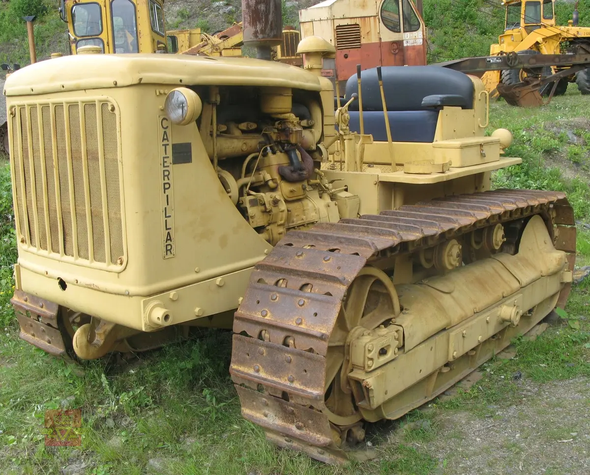 Caterpillar D 7. Gul, (opprinnelig grønn), med svart sete. Maskina er egentlig en bulldozer, men denne er bygget som beltetraktor. Forskjellen ser man best på den bredere fronten hvor det ikke er plasss til hydrauliksylindre for løft av bulldozerskjær. Denne har likevel hatt et skjær, men løfteanordningen som ble benyttet var vinsjen som satt bak på maskina. Wirene gikk fra vinsjen og over to tårn og videre ned på skjæret. Maskina har en 4-sylindret dieseldrevet motor som yter ca 128 Hk. Startmotoren er bensindrevet.
Oppstarting av dieselmotorene er såpass spesiell at den beskrives her:
Starteren er en 2-sylindret bensinmotor. Etter å ha skrudd opp bensinkrana og slått på tenningsbryteren på ON, settes sveiva ned gjennom panseret. Choken må setes på etter behov og gasspjeldet må settes på litt over tomgang. Startmotoren dras over komp. til den starter. Startmotoren bør gå noen minutter fordi avgassene varmer opp dieselmotorens innsugningsrør. Dieselmotorens gasshåndtak settes på halv gass, og dekompresjonshåndtaket på siden av motoren settes til, (slik at motoren går lett rundt).
Det finnes to håndtak for å koble til driften mellom starter og hovedmotor, det ene for å flytte "bendixdrevet" i inngrep med svinghjulet og det andre håndtaket er en clutch som setter i gang bevegelsen av dieselmotoren. Man kjører da noen omdreininger får så å sette dekompresjonshåndtaket i halvstilling. Når man ser på eksosen at dieselen begynner å forbrenne slår man håndtaket over på full kompresjon. Etter noen omdreininger går hovedmotoren av seg selv, slik at starteren kan kobles fri og bensinkrana stenges og tenning slåes av.