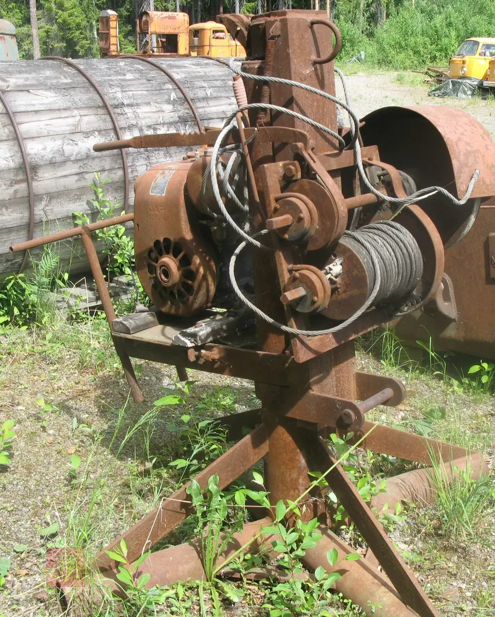 Vinsj for løftekran, står på ramme med tre bein. Kranbommen mangler.
Drives av en 1-sylindret bensinmotor, model 4/3 av fabrikat J.A.P. Merket av produsent.
I rusten tilstand.