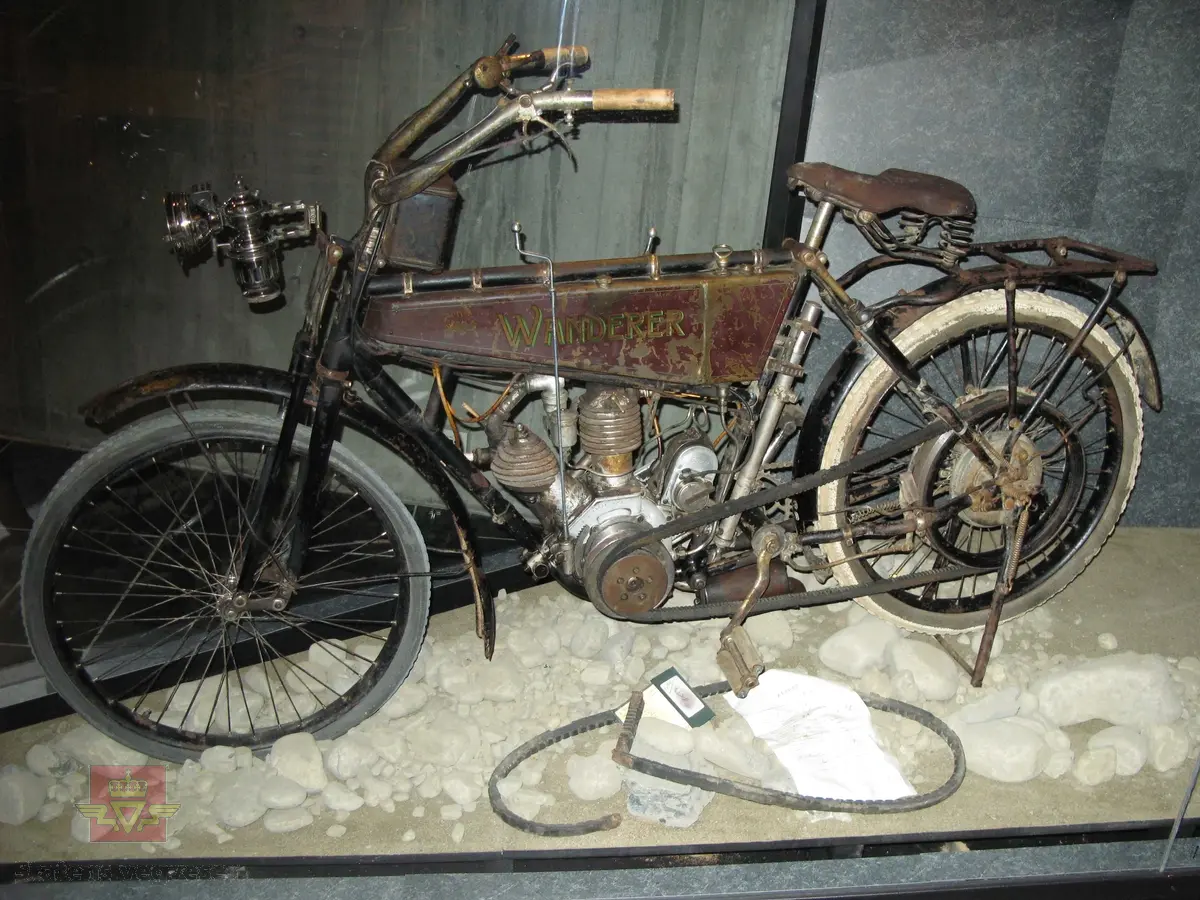Wanderer 3 PS. Tohjuls motorsykkel, svart, brun og grønn med staffering og merking i rødt. Motorsykkelen har en 2-sylindret bensindrevet V-twin motor med sylindervolum 404 cm3 og en ytelse på 3,5 hk. Sykkelen har merking fra produsenten. Det er også et utdatert kjennemerke festet til sykkelen. Dekkdimensjon er 650-55.