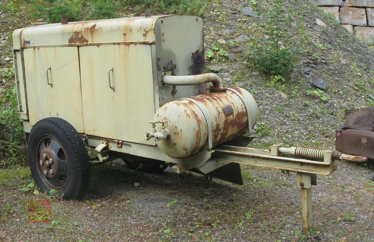 Transportabel kompressor, 1-akslet med 2 luftfyllte gummihjul, (trolig kompaktgummi opprinnelig). Grønn med grønn drivmotor og kompressor. Motoren er en dieseldrevet 4-sylindret to-takts type med kruttstart. Selve kompressordelen er 2-sylindret. Både dieselmotoren og kompressoren er produkter fra Atlas Diesel. Enheten kalles Mono-block, (har felles veivhus og bunnpanne). Vannavkjølt. Kompressoren har drag med støttebein. Merking fra produsent. Antatt kapasitet er 3 kubikkmeter luft i minuttet.