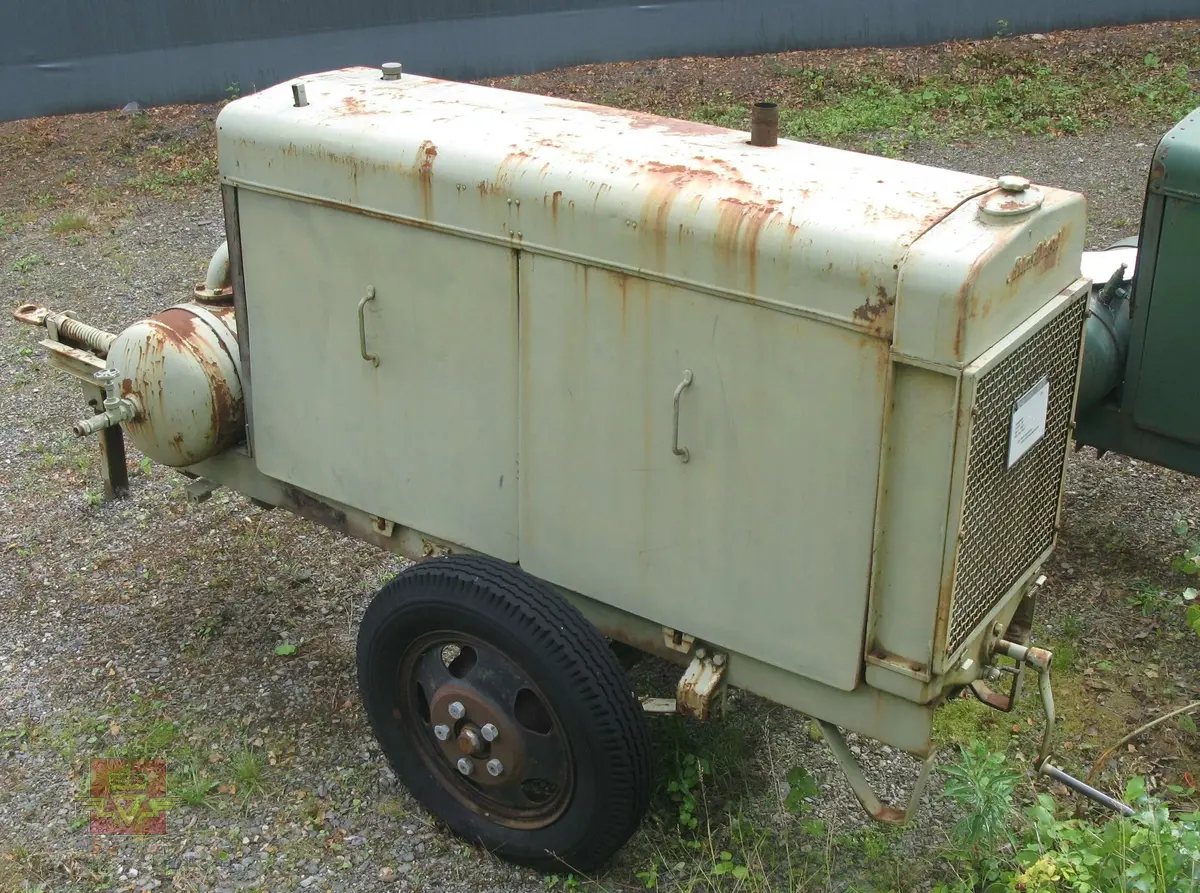 Transportabel kompressor, 1-akslet med 2 luftfyllte gummihjul, (trolig kompaktgummi opprinnelig). Grønn med grønn drivmotor og kompressor. Motoren er en dieseldrevet 4-sylindret to-takts type med kruttstart. Selve kompressordelen er 2-sylindret. Både dieselmotoren og kompressoren er produkter fra Atlas Diesel. Enheten kalles Mono-block, (har felles veivhus og bunnpanne). Vannavkjølt. Kompressoren har drag med støttebein. Merking fra produsent. Antatt kapasitet er 3 kubikkmeter luft i minuttet.