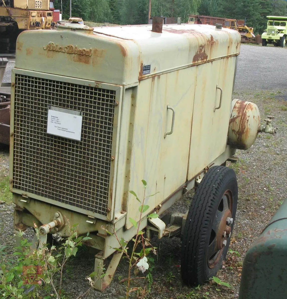 Transportabel kompressor, 1-akslet med 2 luftfyllte gummihjul, (trolig kompaktgummi opprinnelig). Grønn med grønn drivmotor og kompressor. Motoren er en dieseldrevet 4-sylindret to-takts type med kruttstart. Selve kompressordelen er 2-sylindret. Både dieselmotoren og kompressoren er produkter fra Atlas Diesel. Enheten kalles Mono-block, (har felles veivhus og bunnpanne). Vannavkjølt. Kompressoren har drag med støttebein. Merking fra produsent. Antatt kapasitet er 3 kubikkmeter luft i minuttet.