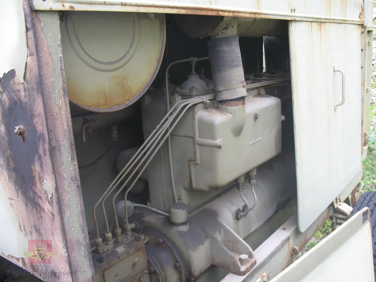 Transportabel kompressor, 1-akslet med 2 luftfyllte gummihjul, (trolig kompaktgummi opprinnelig). Grønn med grønn drivmotor og kompressor. Motoren er en dieseldrevet 4-sylindret to-takts type med kruttstart. Selve kompressordelen er 2-sylindret. Både dieselmotoren og kompressoren er produkter fra Atlas Diesel. Enheten kalles Mono-block, (har felles veivhus og bunnpanne). Vannavkjølt. Kompressoren har drag med støttebein. Merking fra produsent. Antatt kapasitet er 3 kubikkmeter luft i minuttet.