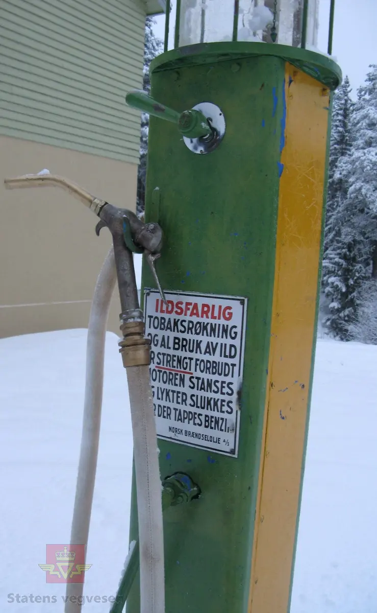 Flerfarget, hovedfarger er grønn og gul, (opprinnelig blå). Håndpumpe og porsjoneringsglass. Står på sokkel. Merking.
Trekasse med lokk høre til pumpa.