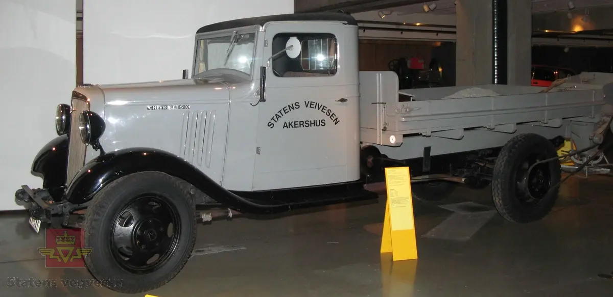 Chevrolet lastebil med tipp plan, sandspreder og plogfeste. Bilen er grå med svarte skjermer, stigtrinn, tak og felger. Brunt sete. Bilen er registrert med kjennemerke: C- 11687. Motoren er en bensindrevet 4-takt, sekssylindret type, trolig med en motoreffekt på 80 Hk. Akselavstand er 157". Nyttelast 2125 kg. Total last 4550 kg.
