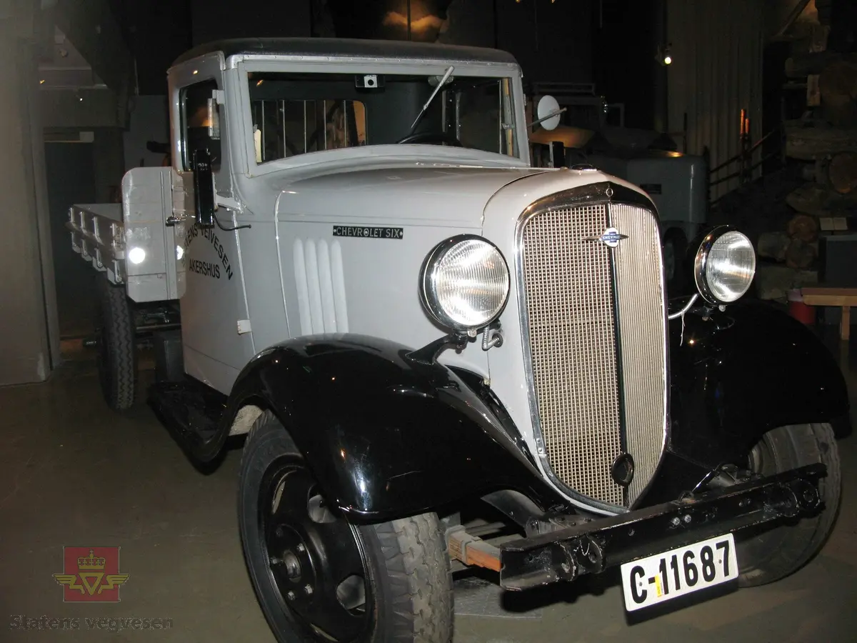 Chevrolet lastebil med tipp plan, sandspreder og plogfeste. Bilen er grå med svarte skjermer, stigtrinn, tak og felger. Brunt sete. Bilen er registrert med kjennemerke: C- 11687. Motoren er en bensindrevet 4-takt, sekssylindret type, trolig med en motoreffekt på 80 Hk. Akselavstand er 157". Nyttelast 2125 kg. Total last 4550 kg.