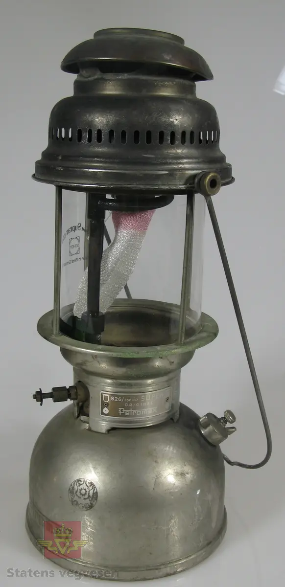 Bærbar parafinlykt av metall og glass. Har ikke veike, men nett.  Lampa fungerer slik at en pumper på trykk, som på en primus.
Merking på glass: Schott Suprax Glas Made in West Germany
Merking på lykt: ORIGINAL Petromax MADE IN GERMANY  REG. 826/350 CP SUPER ORIGINAL Petromax

En eske med ekstra nett følger med, registrert som NVM 00-G-03054-1.