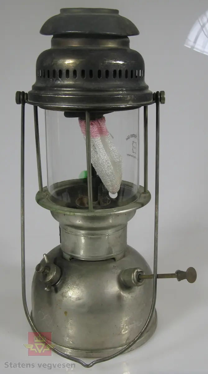 Bærbar parafinlykt av metall og glass. Har ikke veike, men nett.  Lampa fungerer slik at en pumper på trykk, som på en primus.
Merking på glass: Schott Suprax Glas Made in West Germany
Merking på lykt: ORIGINAL Petromax MADE IN GERMANY  REG. 826/350 CP SUPER ORIGINAL Petromax

En eske med ekstra nett følger med, registrert som NVM 00-G-03054-1.