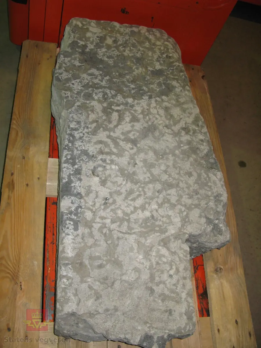 Grå kalkstein i 5 deler. Noe av monogrammet er borte, men 1687 er godt synelig. Kun den største delen er merket. Steinen er lagret på to paller.