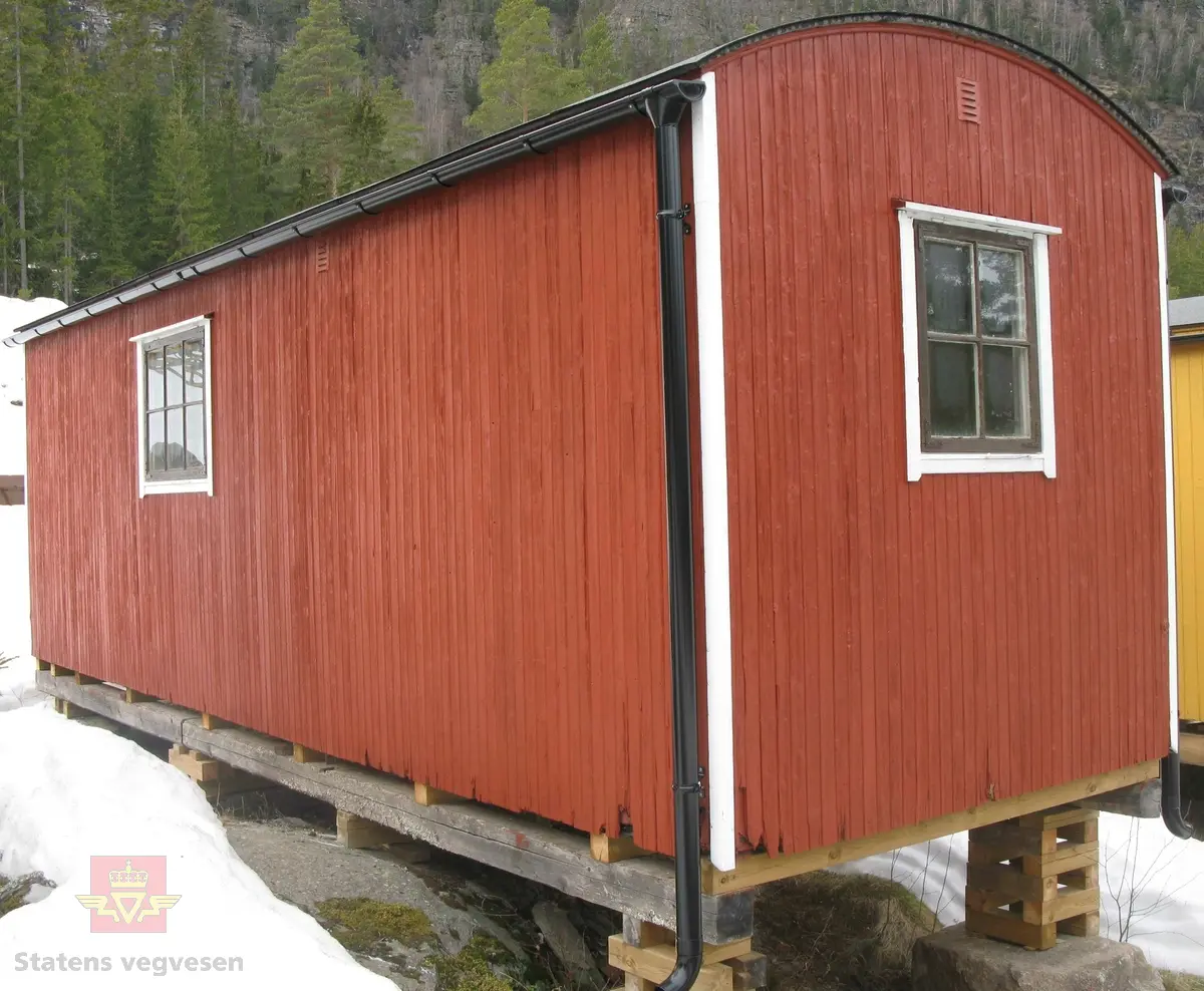 Rød hvilebrakke i tre, med et vindu i hver gavelvegg, ei dør i den ene langveggen og et vindu i den andre langveggen. Dør i gult og vinduskarmer i hvitt og brunt. Stående panel, hjørner har metallbeslag, (i hvitt). Takrenner i stål, (av nyere dato, montert ved NVM). Buet tak kledd med papp. Pipe med hatt. Skjerm over døra. Stigtrinnet ligger inne i brakka. To reflekser på den ene kortveggen. Brakka er innredet med bord, stoler, senger, madrasser, puter, diverse skap og en vedovn av typen Jøtul 380. Blå skap og brunmalt gulv, ellers oljet/lakkert innredning. Hvitt takk innvendig.
