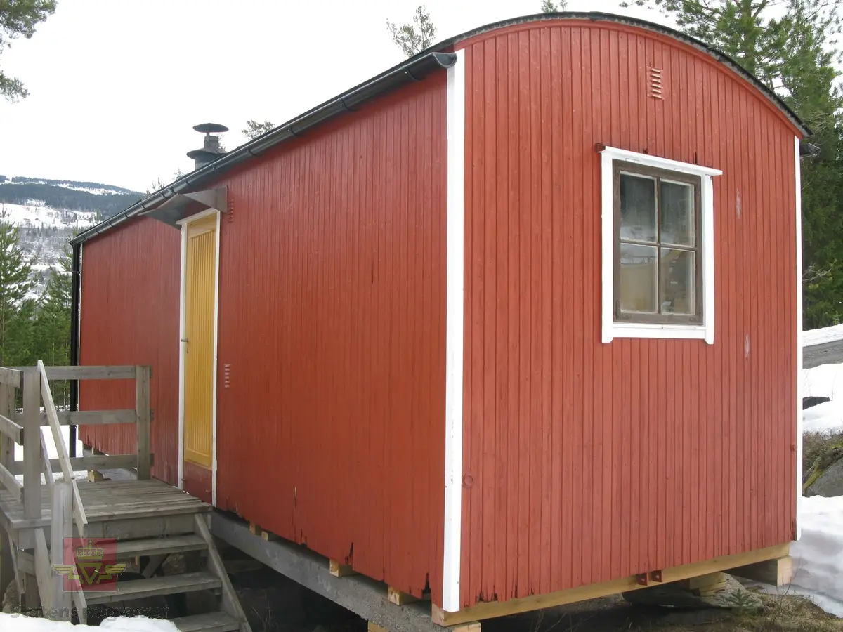 Rød hvilebrakke i tre, med et vindu i hver gavelvegg, ei dør i den ene langveggen og et vindu i den andre langveggen. Dør i gult og vinduskarmer i hvitt og brunt. Stående panel, hjørner har metallbeslag, (i hvitt). Takrenner i stål, (av nyere dato, montert ved NVM). Buet tak kledd med papp. Pipe med hatt. Skjerm over døra. Stigtrinnet ligger inne i brakka. To reflekser på den ene kortveggen. Brakka er innredet med bord, stoler, senger, madrasser, puter, diverse skap og en vedovn av typen Jøtul 380. Blå skap og brunmalt gulv, ellers oljet/lakkert innredning. Hvitt takk innvendig.
