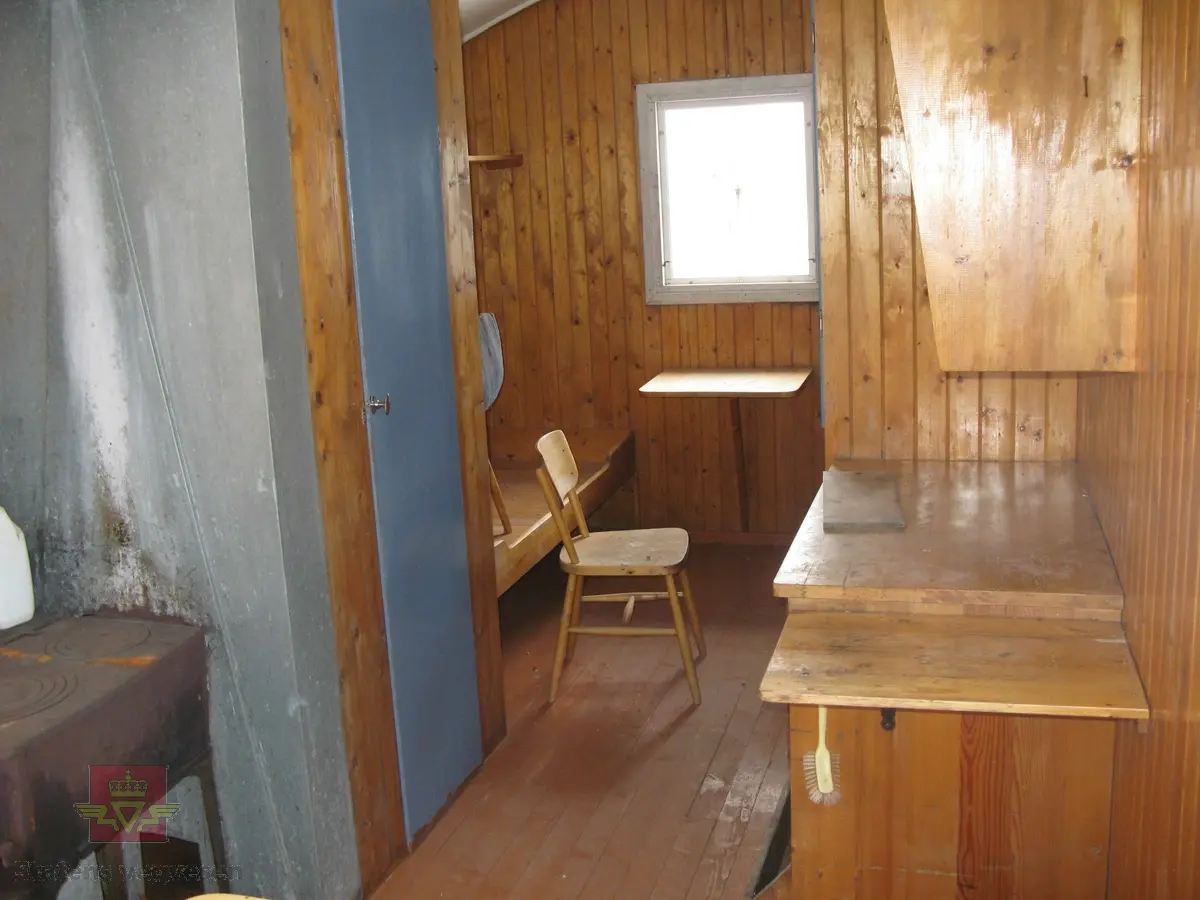 Rød hvilebrakke i tre, med et vindu i hver gavelvegg, ei dør i den ene langveggen og et vindu i den andre langveggen. Dør i gult og vinduskarmer i hvitt og brunt. Stående panel, hjørner har metallbeslag, (i hvitt). Takrenner i stål, (av nyere dato, montert ved NVM). Buet tak kledd med papp. Pipe med hatt. Skjerm over døra. Stigtrinnet ligger inne i brakka. To reflekser på den ene kortveggen. Brakka er innredet med bord, stoler, senger, madrasser, puter, diverse skap og en vedovn av typen Jøtul 380. Blå skap og brunmalt gulv, ellers oljet/lakkert innredning. Hvitt takk innvendig.
