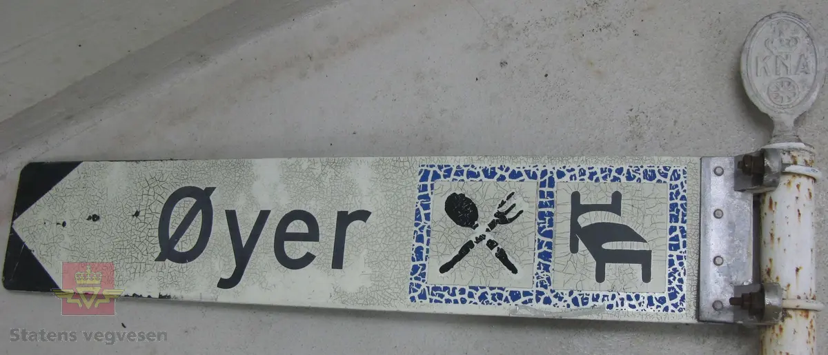 Hvitmalt stolpe, (stålrør), med tre metall-skilt, (aluminium), montert på. På toppen av stolpen sitter et ovalt "KNA-skilt" av, med flens som går innvendig i stolpen. Stolpen har et vegviser skilt av påskrudd, skiltet har symbol for bespisning og overnatting, og teksten "Øyer". Det tredje skiltet på stolpen er uleselig, all tekst mangler. 

