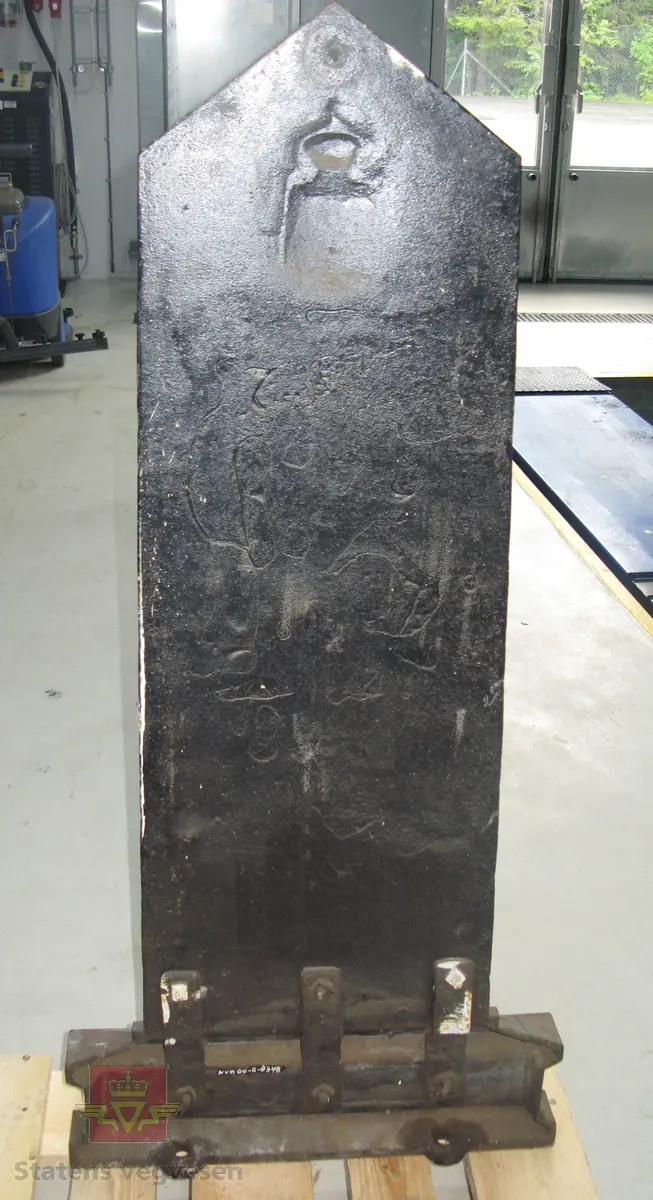 Kilometertavle, (skilt), lagd av støpejern, med riksvåpenmotiv og teksten:" SMAALENENES AMT 90 KILOMETER FRA KRISTIANIA RØDENÆS". Svart bunnfarge, tekst i gull. Baksiden har teksten: "MOSS JERNSTØBERI".