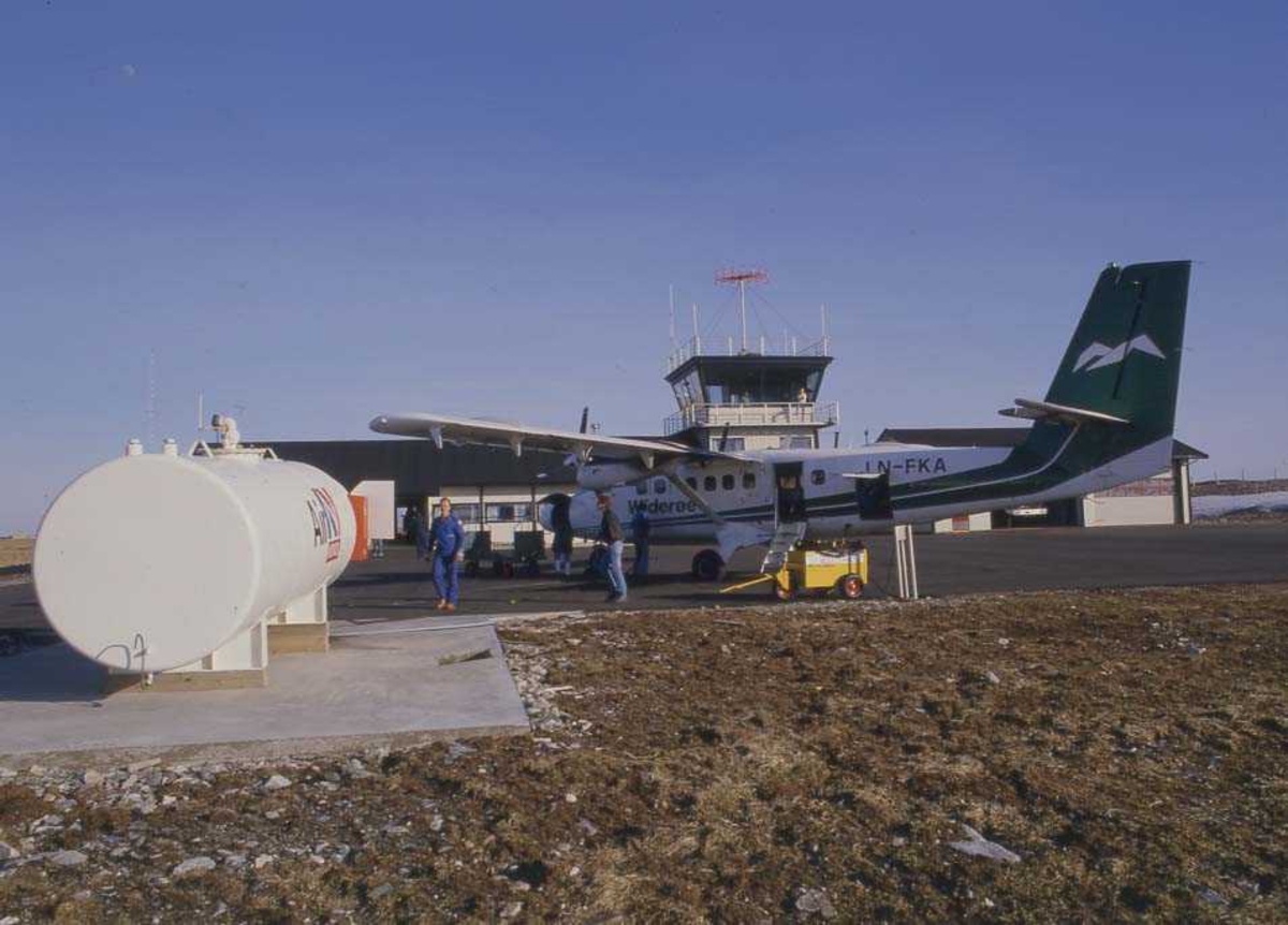 Lufthavn/Flyplass. Røst. Et fly, LN-FKA, DHC-6 Twin Otter fra Widerøe står parkert ved Ekspedisjonen/Flytårnet. I bakgrunnen fjell på Værøy.