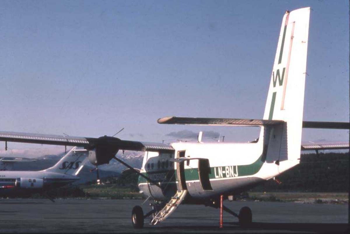 Lufthavn/flyplass. Tromsø/Langnes. Et fly, LN-BNJ, DHC-6-300 Twin Otter fra Widerøe parkert, klar til å ta mot nye passasjerer. 2 fly fra SAS, DC-9 `ere ses i bakgrunnen.