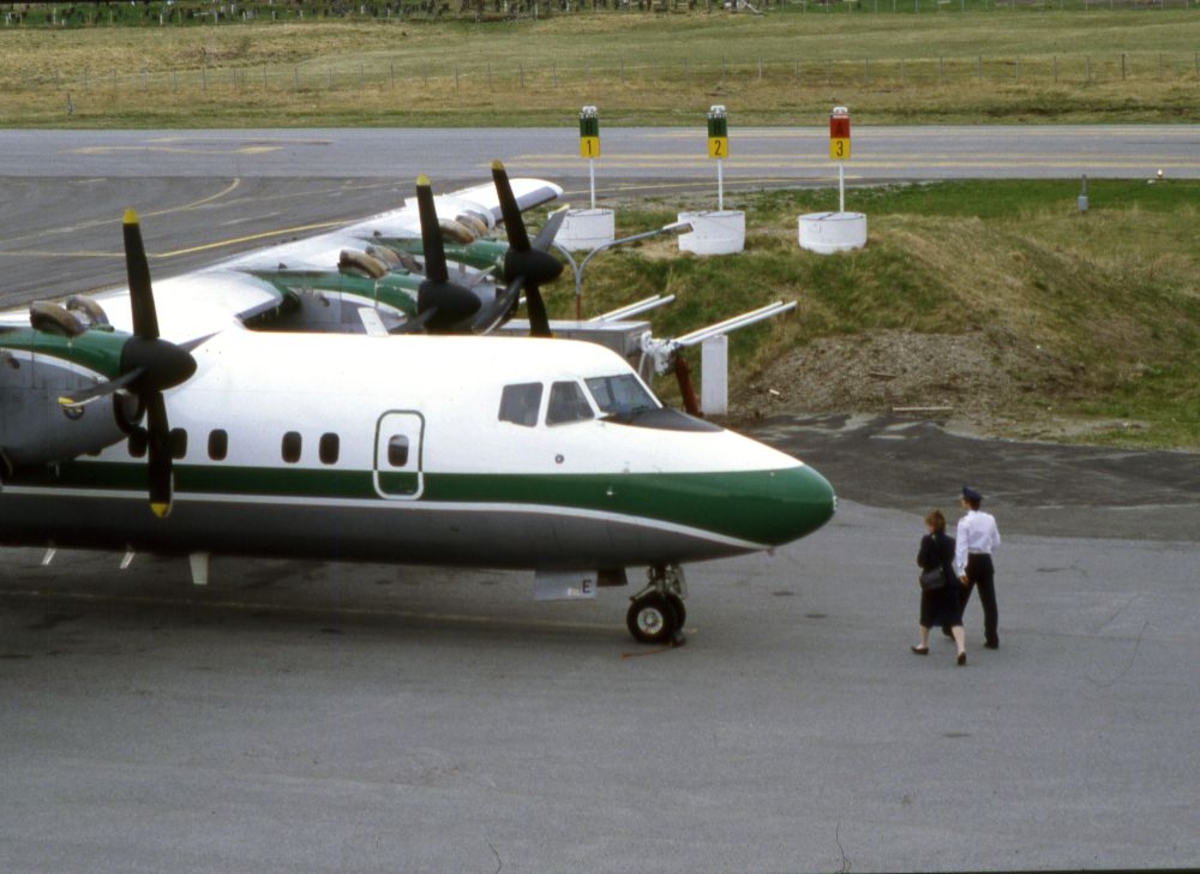 Lufthavn (flyplass). Et fly, LN-WFE, DHC-7-102, Dash7 fra Widerøe. To personer (pilot og kabinansatt) foran flyet.