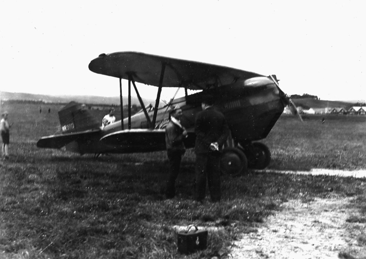 Åpen plass, lufthavn, to personer foran ett fly på bakken, Curtiss Hawk, P-6A.   Reg.nr NR 9110.