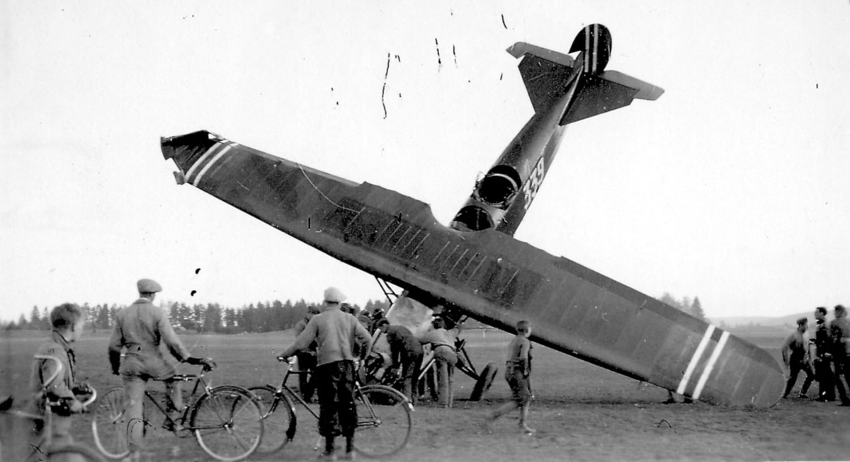 Åpen plass, ant. lufthavn. Ett fly, Fokker CVE, nr 339  står med nesepartien ned i bakken, havari. Flere personer ved flyet.