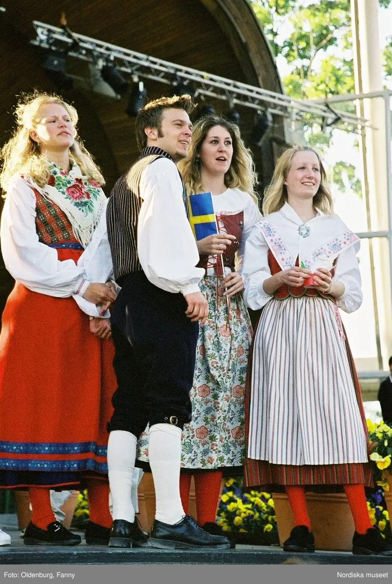 Firandet av den svenska nationaldagen den 6 juni 2004 på Skansen. Människor iklädda folkdräkt. Näsby Parks Scoutkår. Blomsterarrangemang.