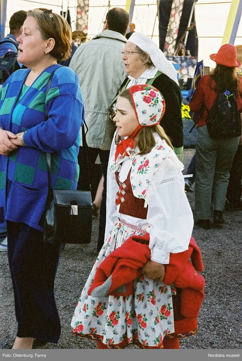 Firandet av den svenska nationaldagen den 6 juni 2004 på Skansen. Människor iklädda folkdräkt. Näsby Parks Scoutkår. Blomsterarrangemang.