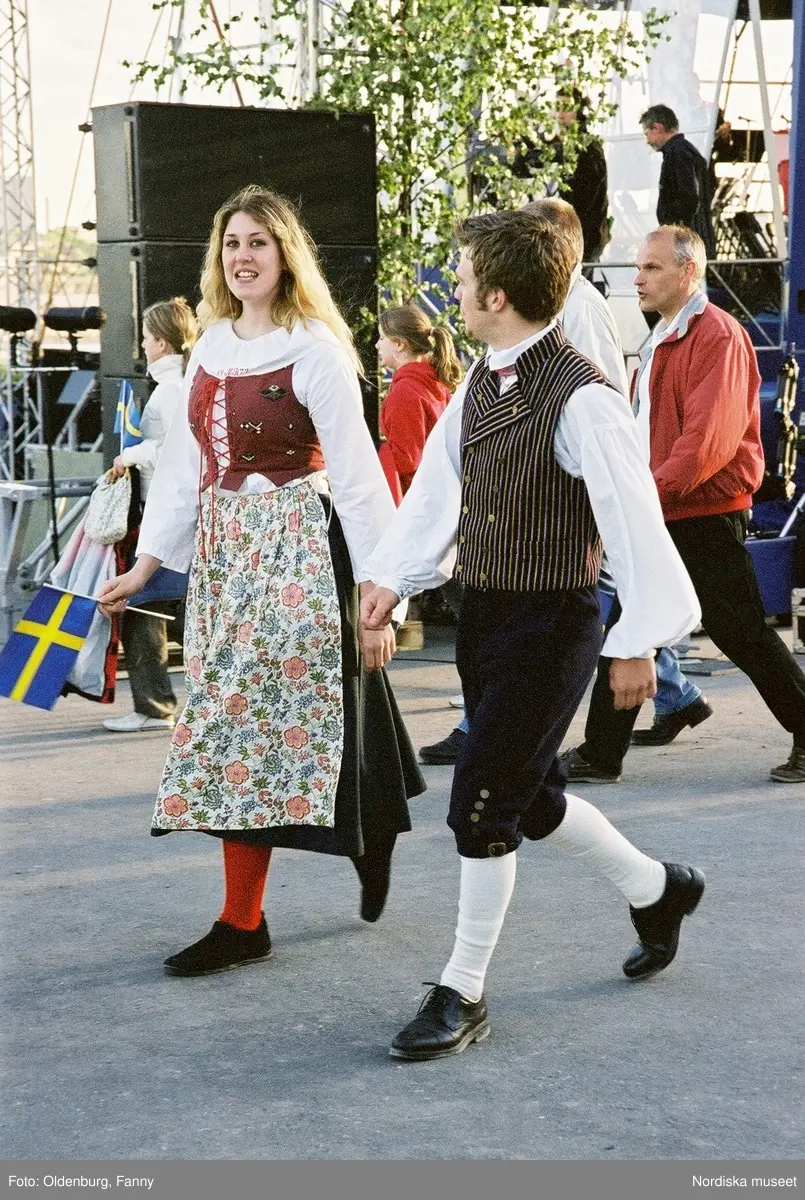 Firandet av den svenska nationaldagen den 6 juni 2004 på Skansen. Människor iklädda folkdräkt. Näsby Parks Scoutkår. Blomsterarrangemang.