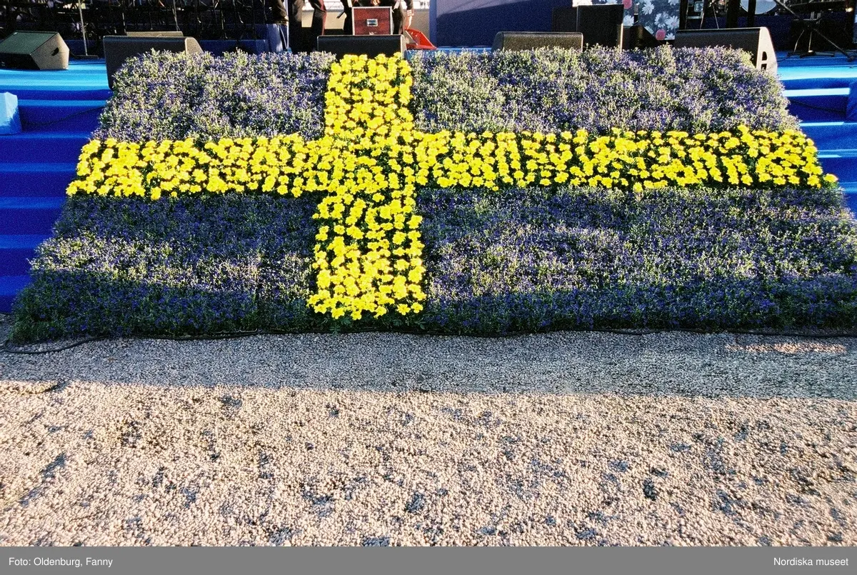 Firandet av den svenska nationaldagen den 6 juni 2004 på Skansen. Människor iklädda folkdräkt. Näsby Parks Scoutkår. Blomsterarrangemang.