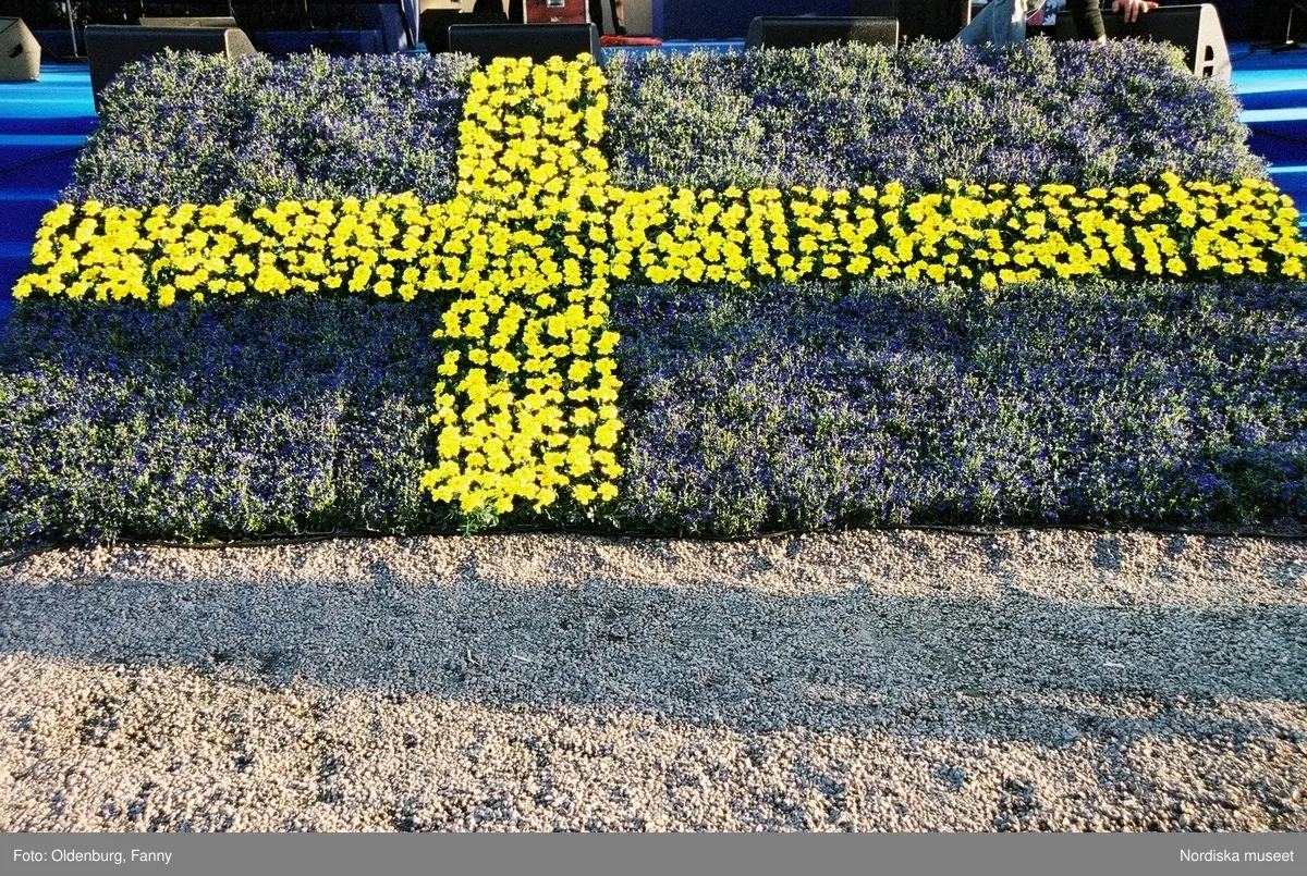 Firandet av den svenska nationaldagen den 6 juni 2004 på Skansen. Människor iklädda folkdräkt. Näsby Parks Scoutkår. Blomsterarrangemang.