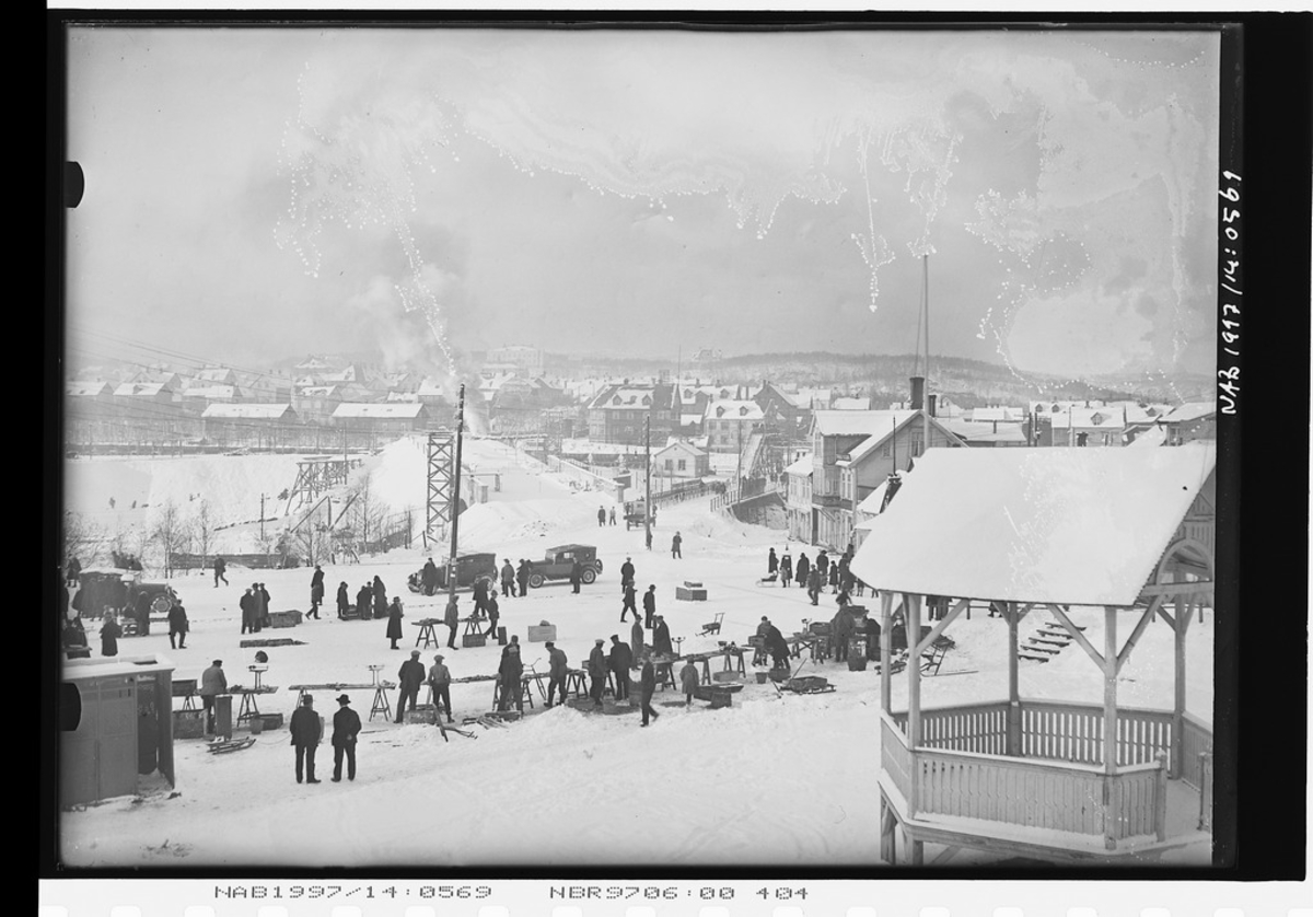 Narvik torv med paviljong og fiskehandlere langs Kongens gate. Frydenlundsbrua under bygging. Ofotveien med "Sukkenes bro". Det grønne hus (toalet) foran til v.