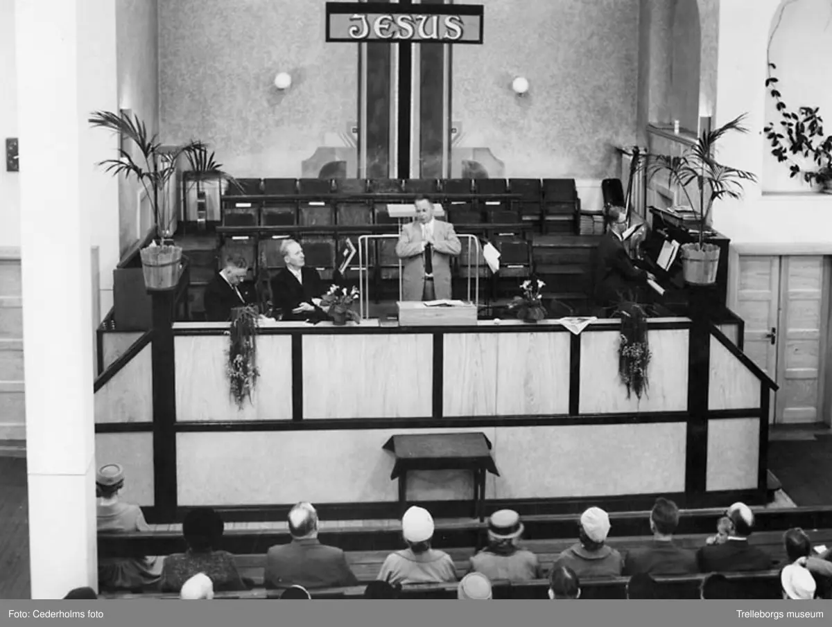 Elimförsamlingen. Interiör från kyrkan på Valldammsgatan 2. På podiet  sitter Willis Säwe och Ernst Almqvist. Einar Ekberg leder bönen.