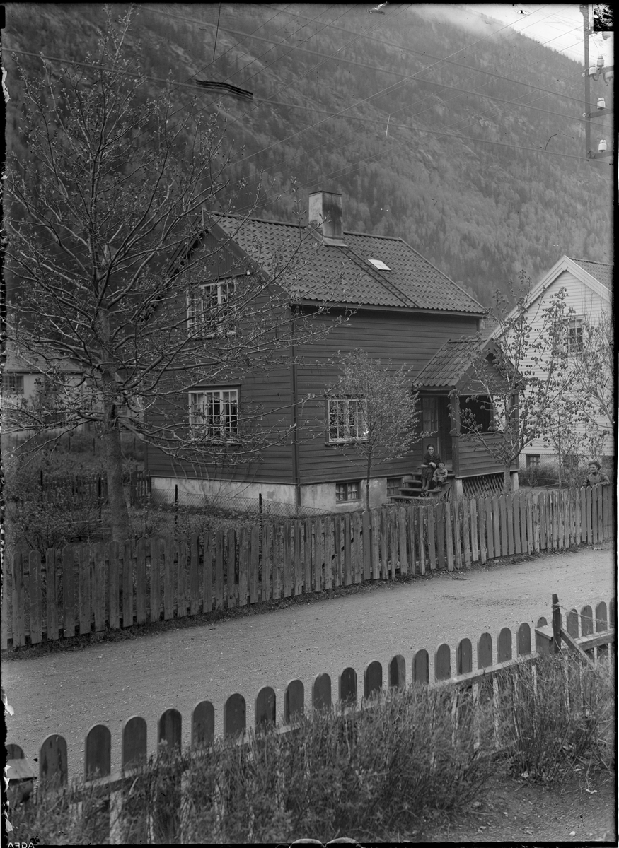 Boliger, Egne Hjem, Ingeniør Waadensgate 7. Kvinne og barn sittende på trappa foran husets inngangsparti. Kvinne stående lent mot tregjerde i hagen mot veien.